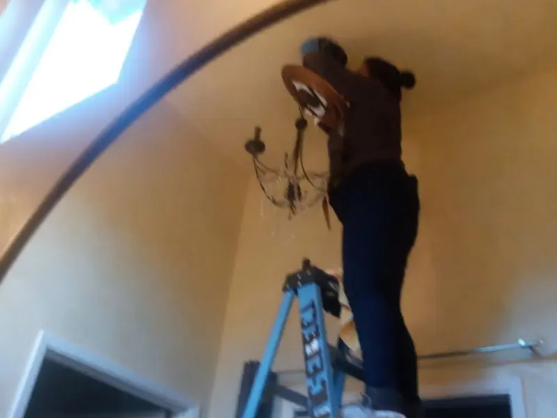 Electrician installing a chandelier in a Clay residence